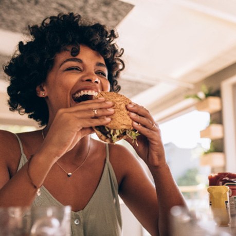 Woman smiling while eating burger at restaurant