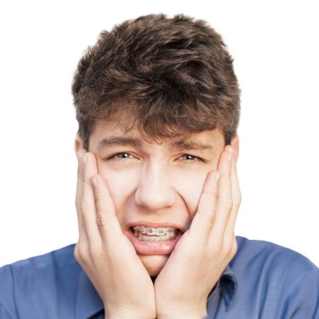 A young teenage male holding his face between his hands while cringing in pain because of his braces
