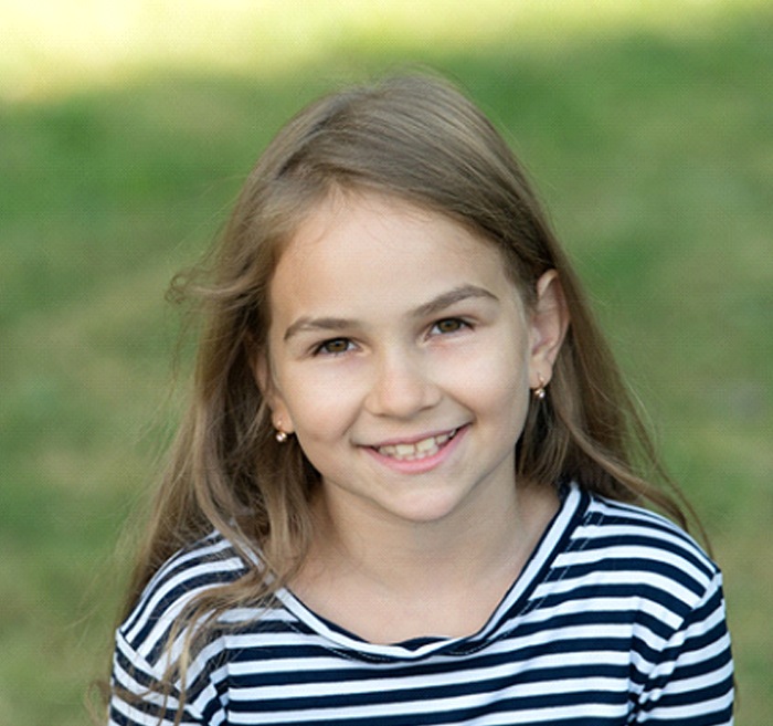 A little girl wearing a striped blouse and smiling after receiving Phase One Orthodontics in Cumming