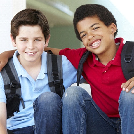 Two young boys wearing backpacks outside of school and one wearing braces in Cumming