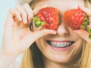 Smiling girl with braces holding strawberries follows tips from Cumming, GA orthodontist