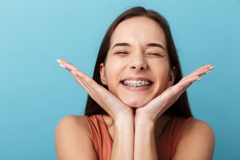 a young woman holding her head between her hands and smiling while wearing metal braces