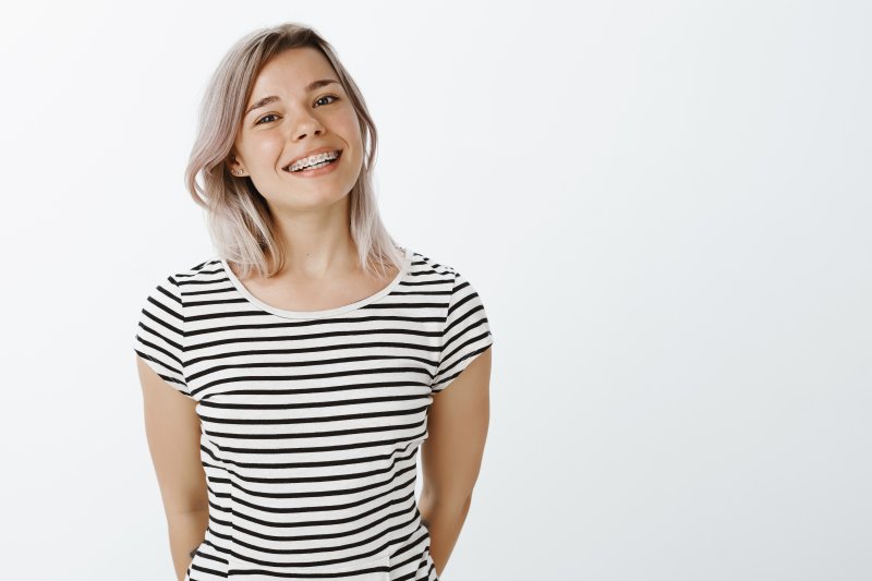 a young woman wearing a striped shirt and braces stands and smiles to show off her healthy, perfectly aligned teeth