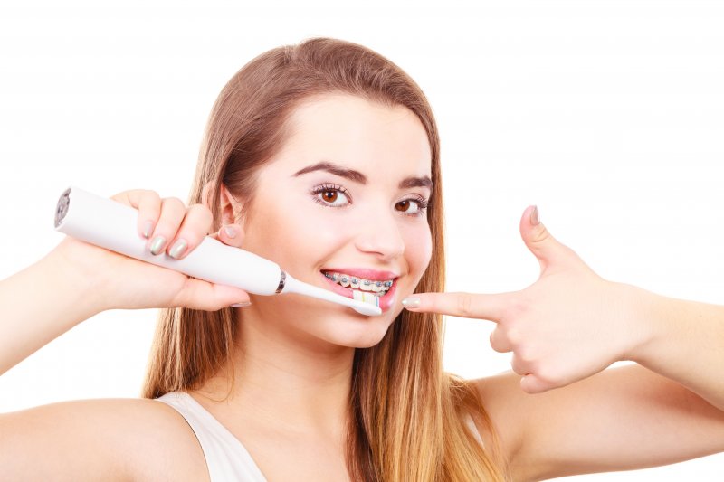 a young woman using an electric toothbrush to clean her teeth and braces in Cumming