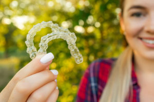 a teen standing outside and holding two clear aligners