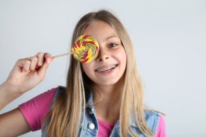 smiling young girl with braces holding a lollipop