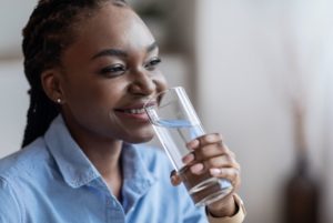 Professional woman in blue collared shirt with braces smiling and drinking a glass of water