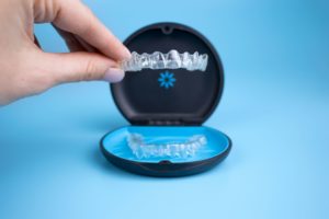 Closeup of Invisalign aligners in their case with a hand holding up one of the trays