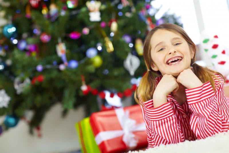 A girl showing off her braces with a smile under the Christmas tree