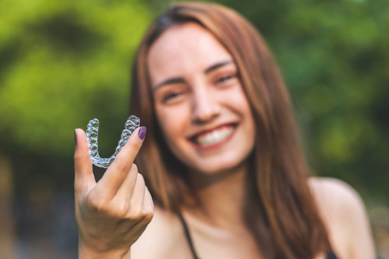 A woman holding an Invisalign aligner at a distance from her face