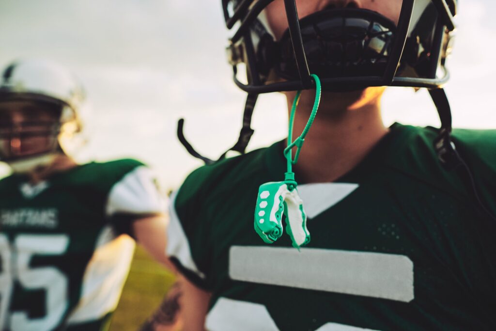 Nose-to-chest view of teen in green football gear with mouthguard