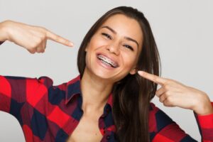 Woman with braces pointing to her smile