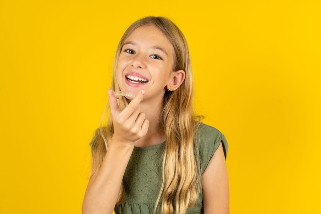 Girl in green shirt holding Invisalign with yellow background