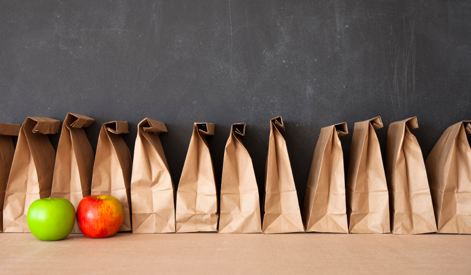 Brown bag lunches lined up with a red and green apple