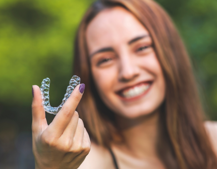 Woman smiling, holding clear aligner