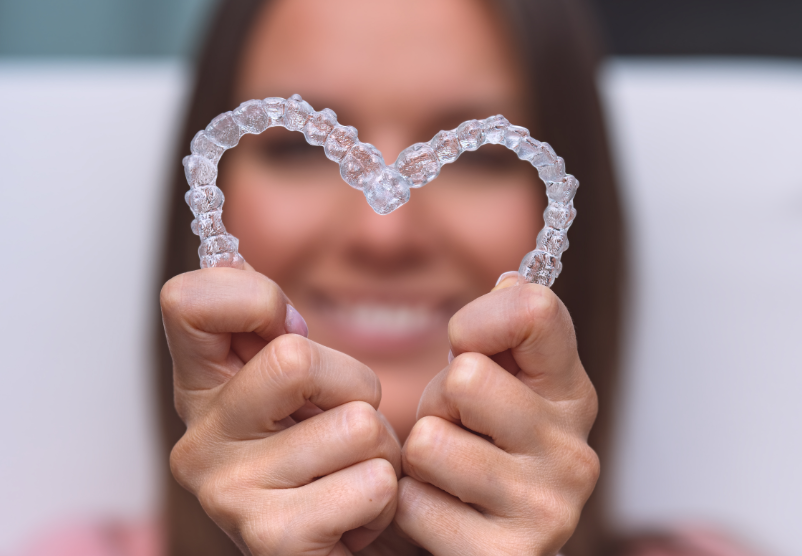 Woman holding clear aligners in the shape of a heart