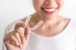 Woman in white shirt smiling holding Invisalign