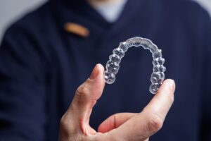Man in navy shirt holding Invisalign in thumb and forefinger